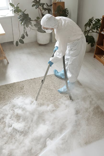 A person performing surface cleaning with a vacuum cleaner on a patterned rug inside a residential living room. The individual is wearing casual clothing, including a beige jacket, dark jeans, and whi